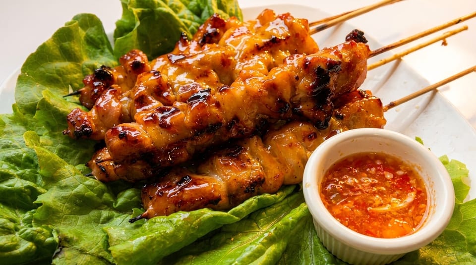 Grilled chicken skewers with a sweet glaze, served on lettuce with a side of chili sauce.