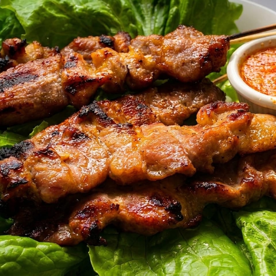Grilled pork skewers with a side of chili dipping sauce, served on a bed of fresh lettuce.