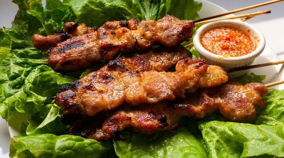Grilled pork skewers with a side of chili dipping sauce, served on a bed of fresh lettuce.